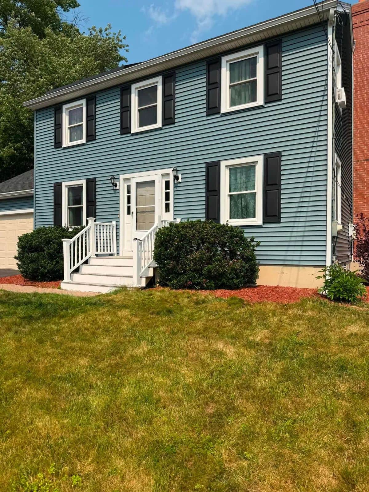 Two-story colonial in Gardner, MA with new blue clapboard siding, black shutters, and white trim