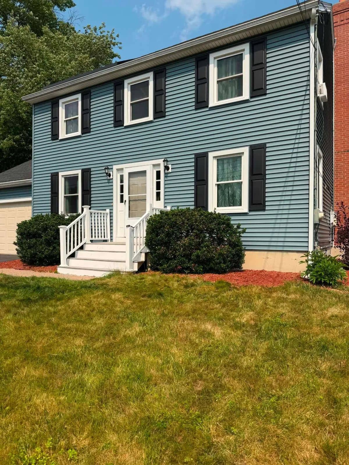 Two-story colonial in Gardner, MA with new blue clapboard siding, black shutters, and white trim