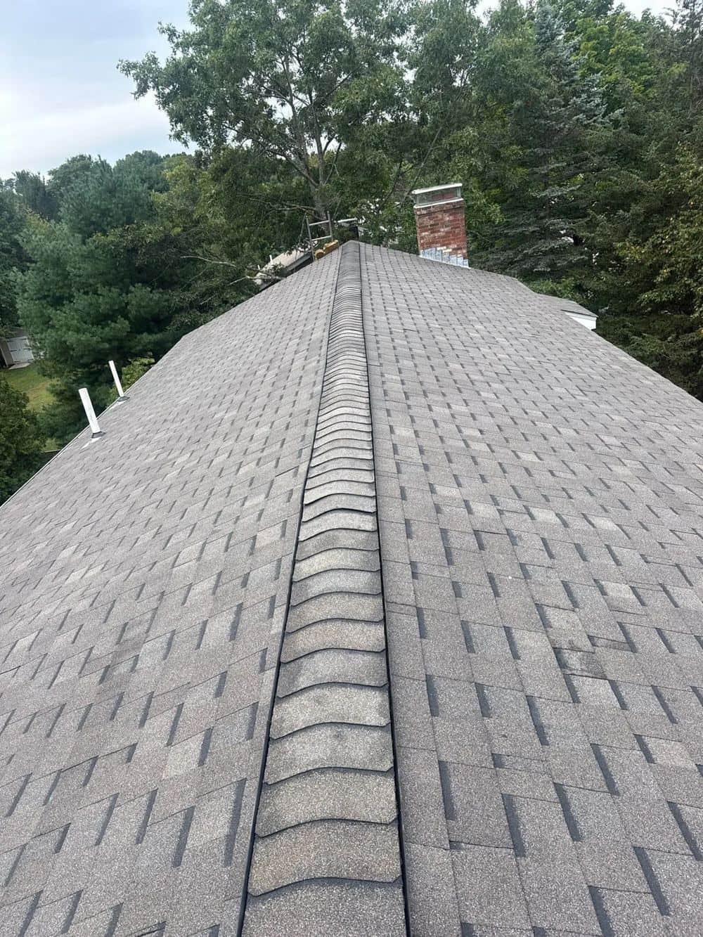 View up a new gray shingle roof toward the ridge and chimney in Medfield, MA