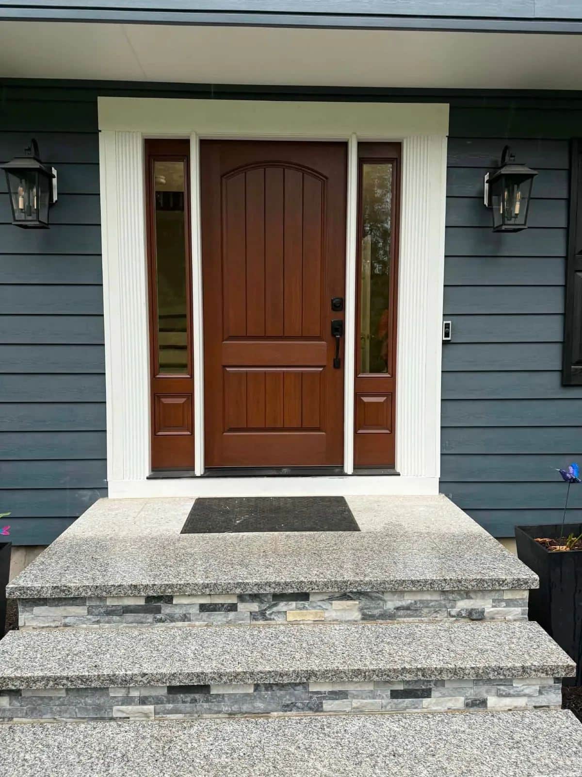 Front entry of a Sudbury, MA home with new dark blue clapboard siding, white trim, and a wood front door