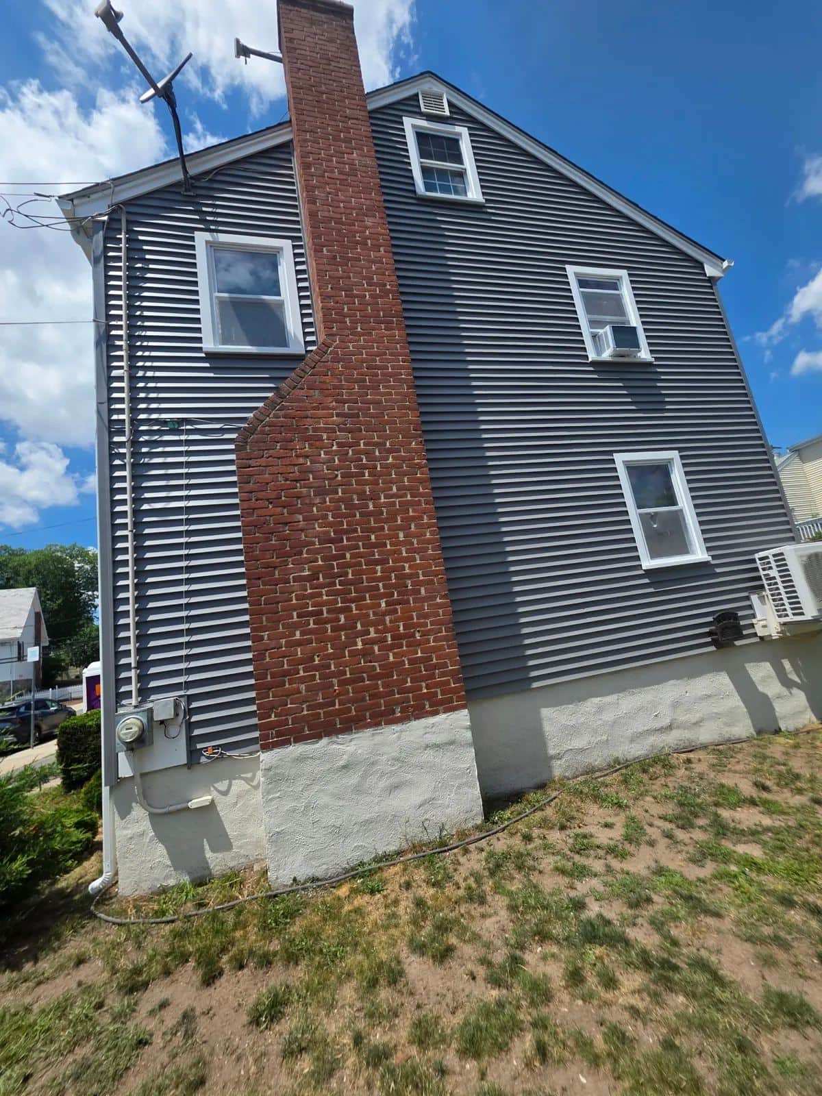 Side of a West Roxbury, MA home with new gray clapboard siding beside a brick chimney