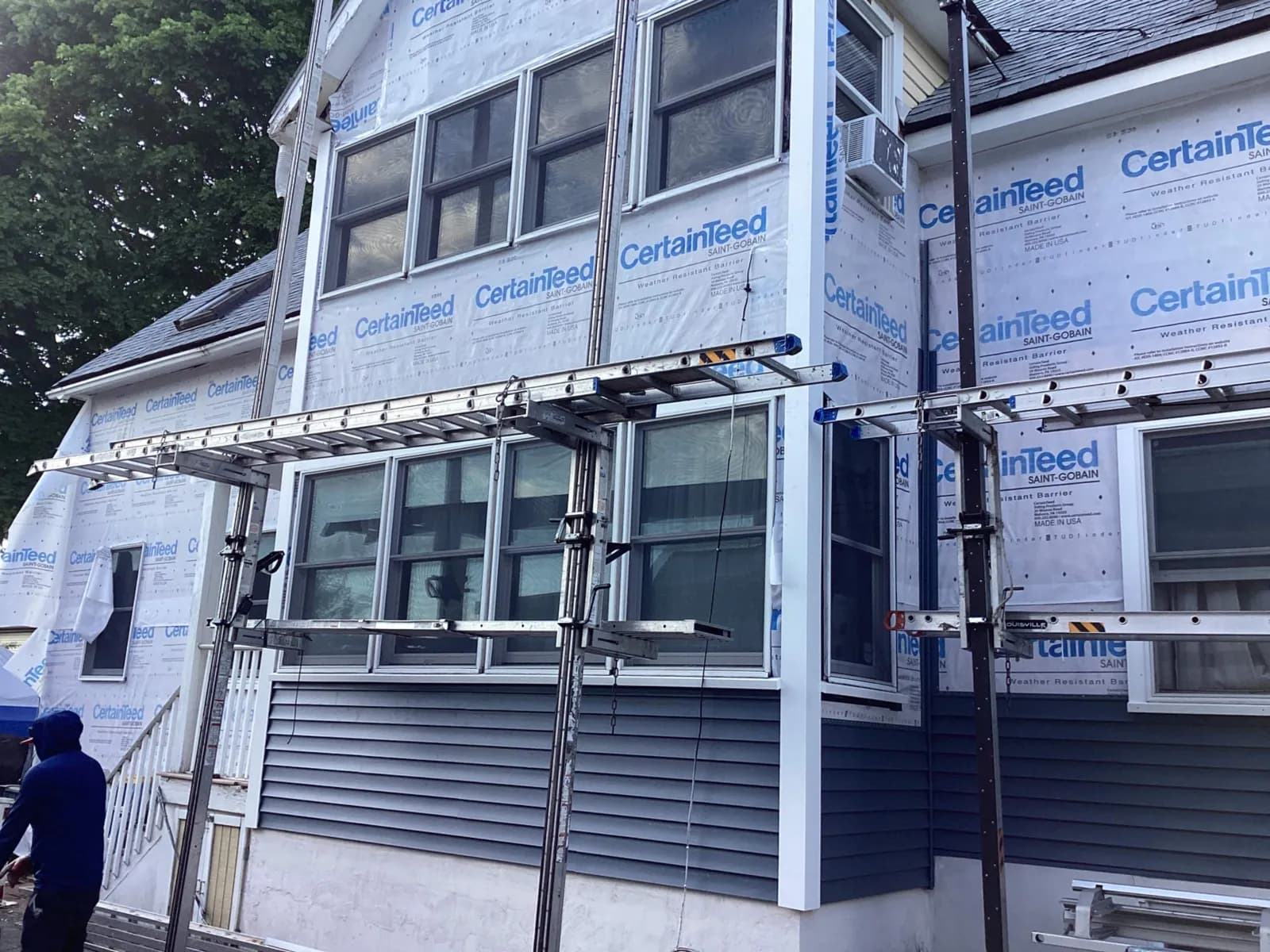 Siding installation in progress: CertainTeed weather-resistant barrier wrapped over the whole house, new white window trim, and the first courses of navy lap siding going up