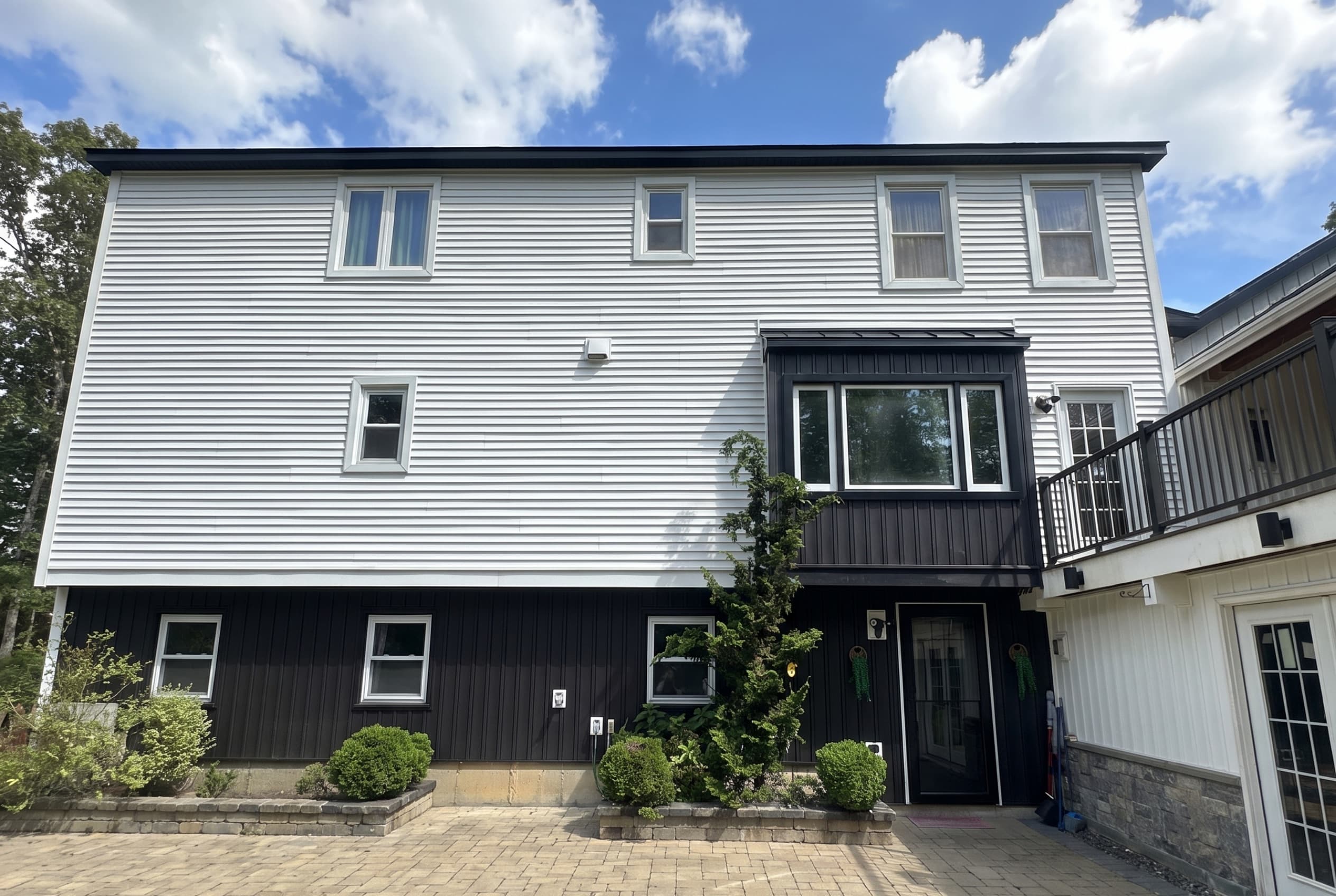Two-tone New England home with white lap siding above and black board-and-batten below, over a paver patio