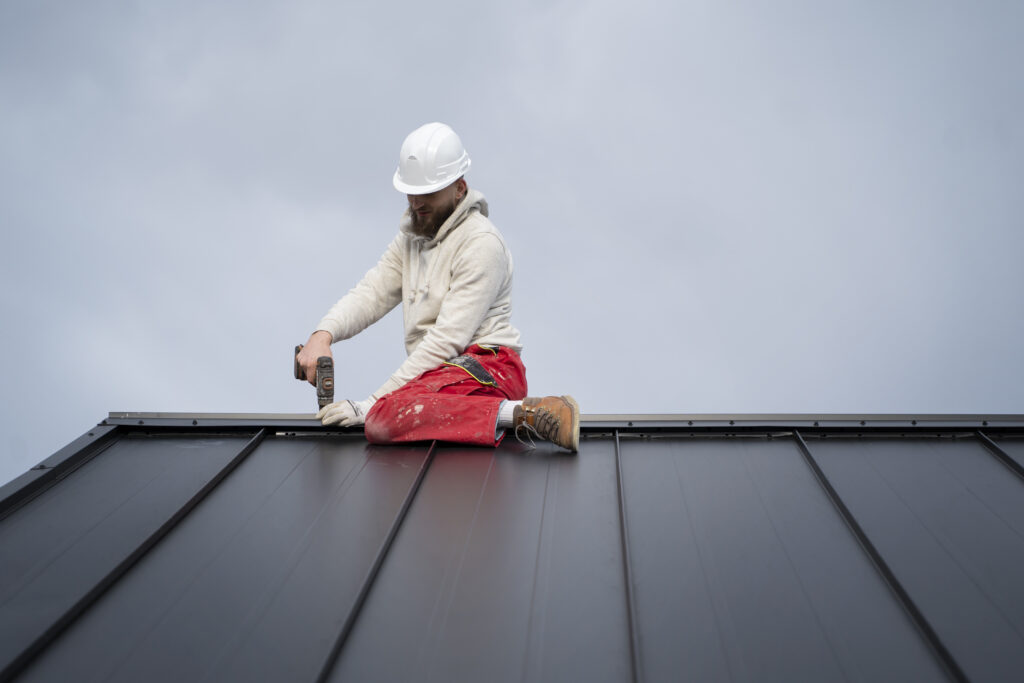 Professional roofer in safety gear installing a black metal roof with a drill, demonstrating precision craftsmanship and focus on durability.