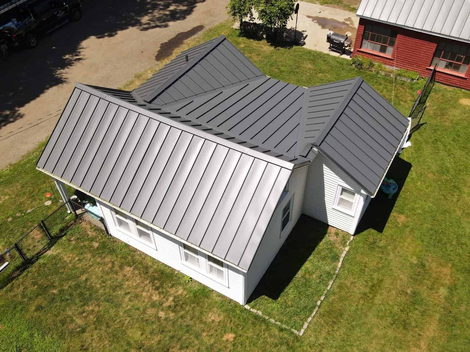 Metal roof on a small white house with multiple pitched sections, reflecting modern roofing materials and durable design.