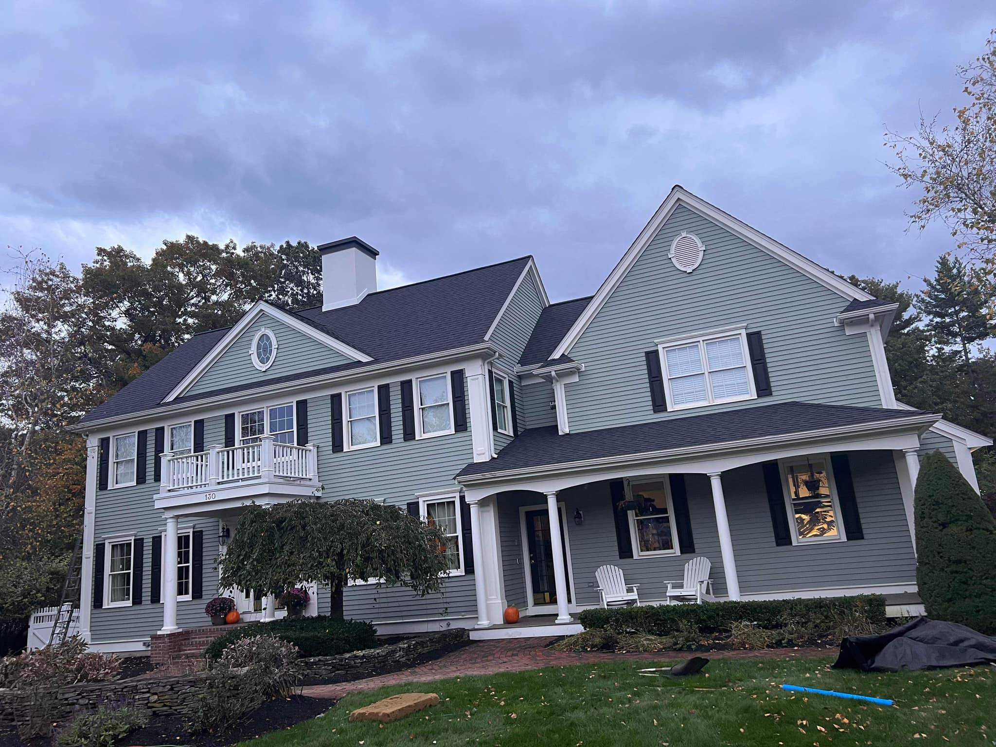Roof with asphalt shingles and house exterior featuring siding, windows, shutters, and a porch with chairs, showcasing residential roofing and home exterior features.
