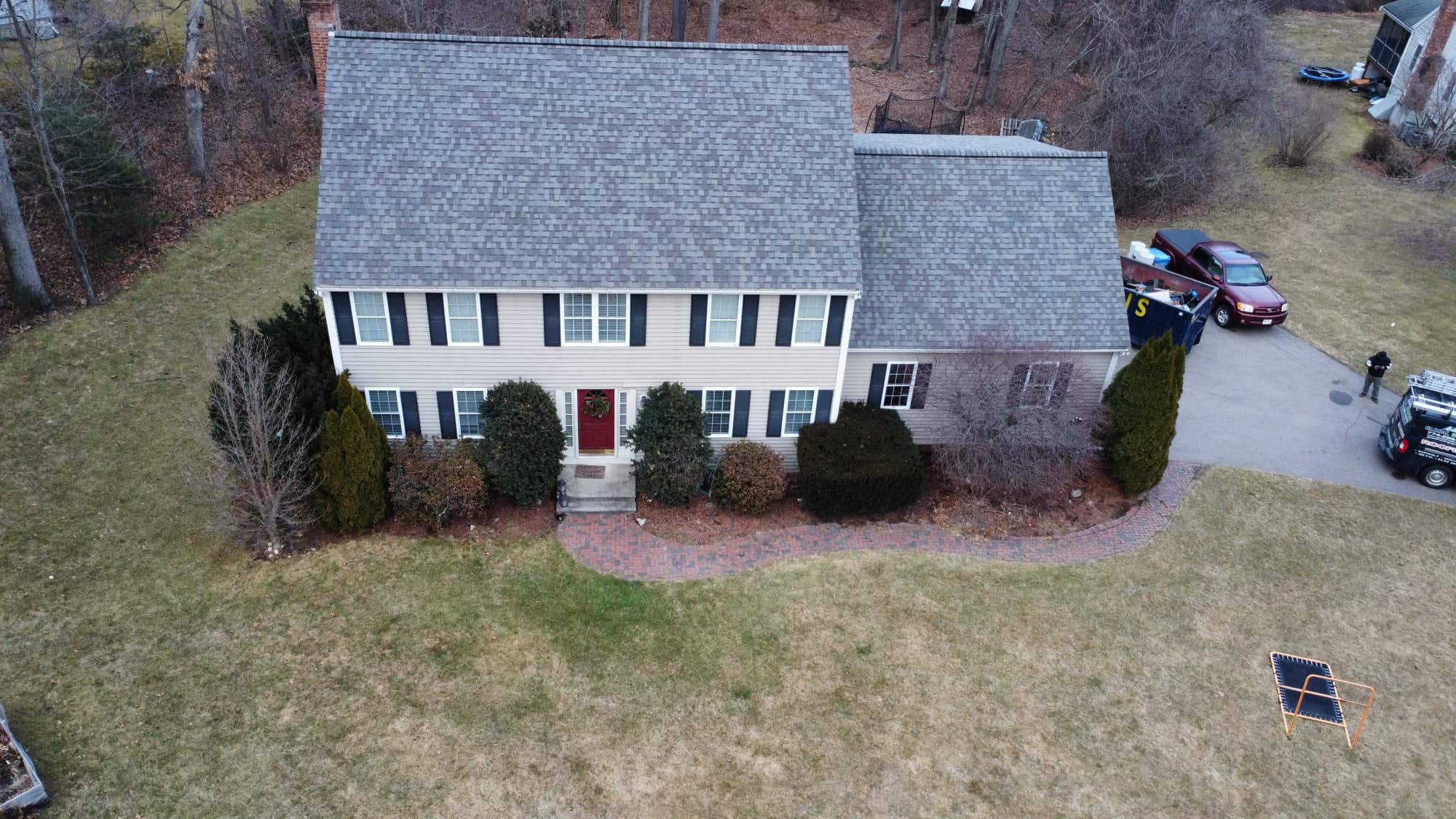 Aerial view of a residential house with a gray shingle roof, surrounded by trees and a well-maintained yard, demonstrating roofing design and home exterior features.