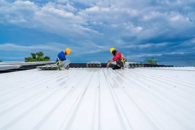 Roof installation workers installing metal roofing panels on a building.