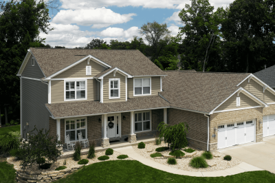 Roof replacement, residential home with beige siding, asphalt shingle roof, landscaped yard, front porch, white garage doors, and lush greenery.